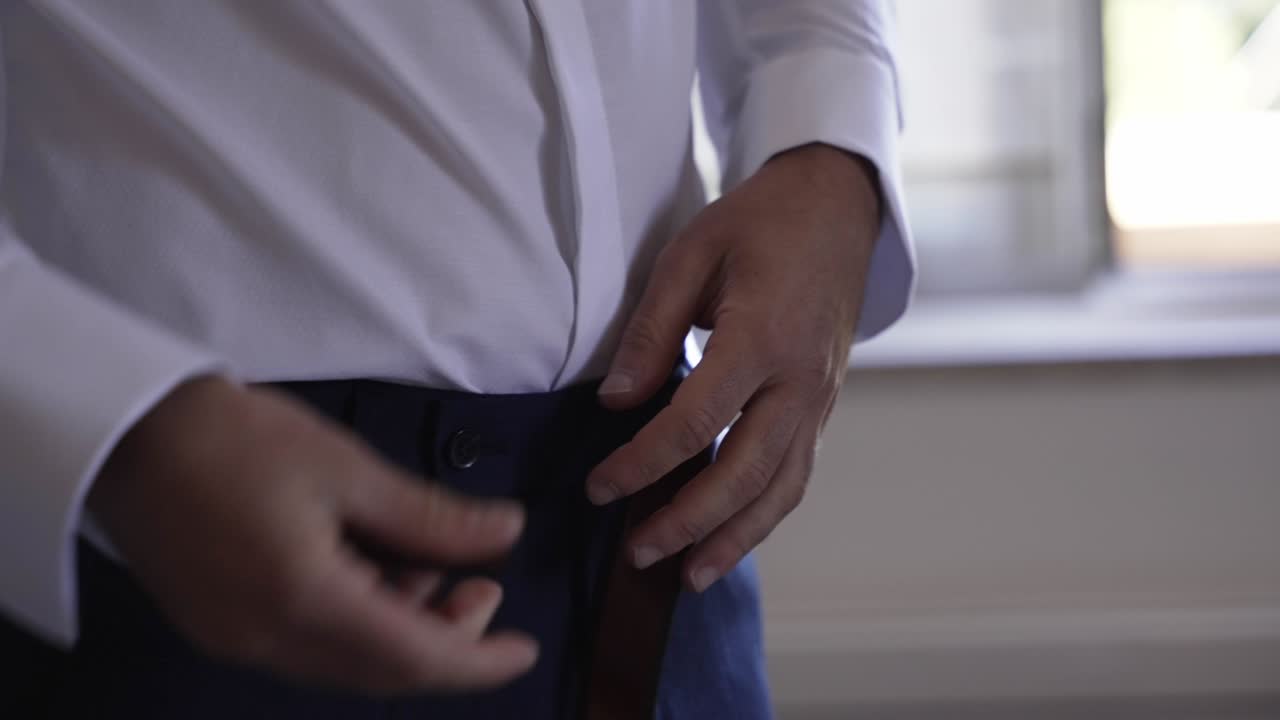 색 드레스 셔츠를 입고, 허리에 어두운 가죽 벨트를 고, 공식적인 행사에 준비하는 남자