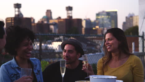 happy friends talk and drink at a table on brooklyn rooftop