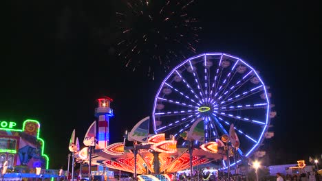 fireworks explode in the night sky behind a ferris wheel at a carnival or state fair 1