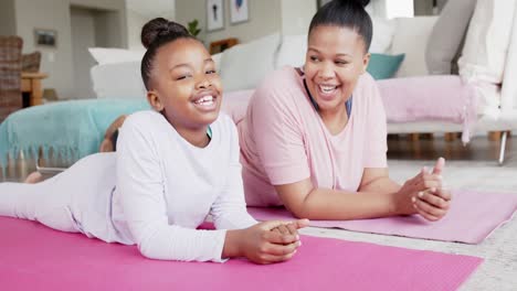 happy unaltered african american mother and daughter lying on yoga mats talking, in slow motion