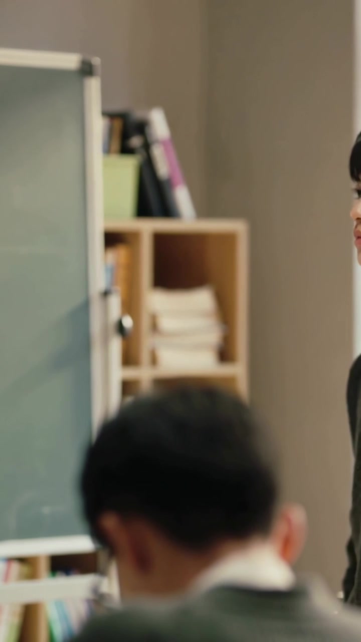 Vertical video: Entering left teacher pacing front class by board asking student answer, copy space