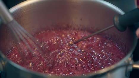 confectioner boils sweet red caramel in metal saucepan