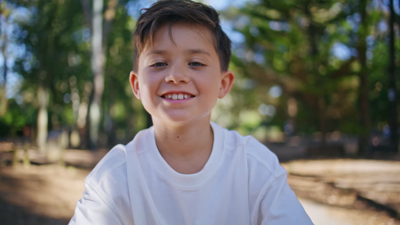 Cheerful kid looking camera at sunshine forest portrait. Happy child at park