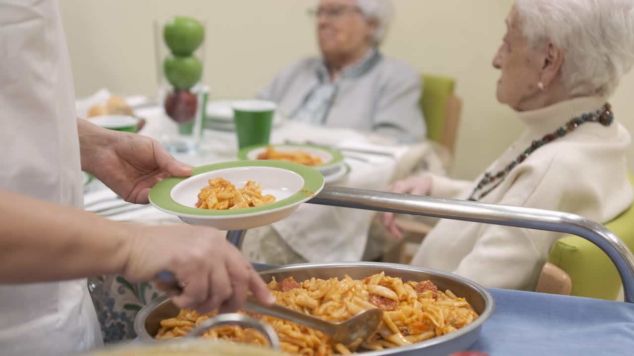 Crop worker serving pasta in plate for elderly people