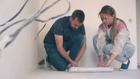 happy family unrolls sheet of wallpaper on floor in room