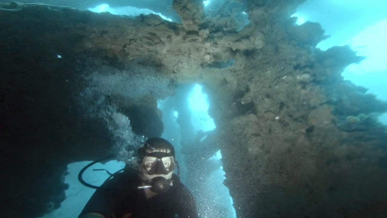 un buzo buceando a través de espacios reducidos de un viejo naufragio en aguas azules profundas, iluminando su camino con una antorcha