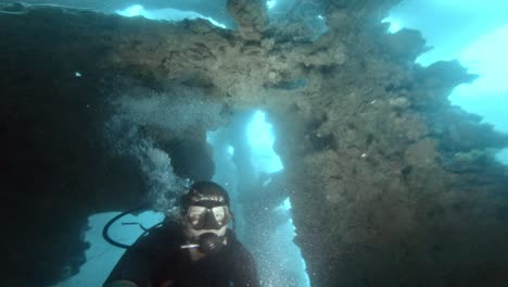 Ein-Taucher-Taucht-Durch-Enge-Räume-Eines-Alten-Schiffswracks-In-Tiefblauem-Wasser-Und-Beleuchtet-Seinen-Weg-Mit-Einer-Taschenlampe