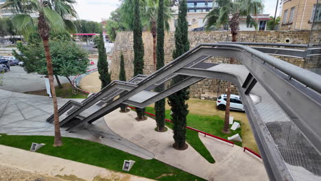 An innovative architectural structure in Nicosia, Cyprus, featuring a unique bridge design surrounded by palm trees and green spaces, captured in slow motion