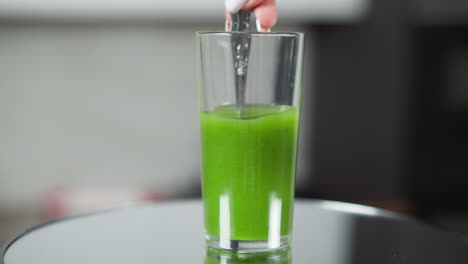 finger dipping into a glass of green smoothie, with a reflection on a glass table