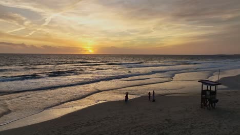 gente viendo la puesta de sol debajo del horizonte frente a la torre de socorristas en la playa