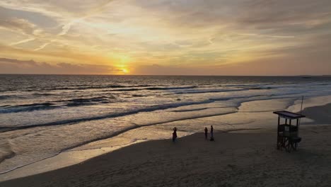 people watching sun set below the horizon in front of life guard tower on beach