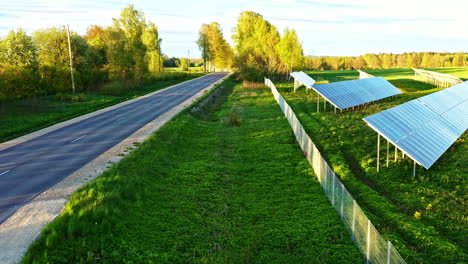 solar panel farm aligned near countryside road and green field at golden hour