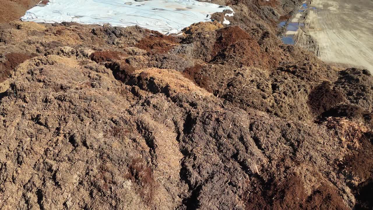 Aerial footage captures expansive mulch and dirt piles on a farm, showcasing texture and scale under bright daylight