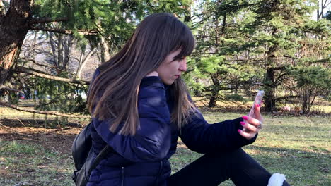 cámara lenta de una joven tomando selfies con un smartphone usando una cámara frontal sentada en el suelo en un parque urbano