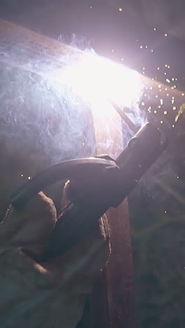 close view man in protective mask welds parts of fence bottom among green bushes in evening