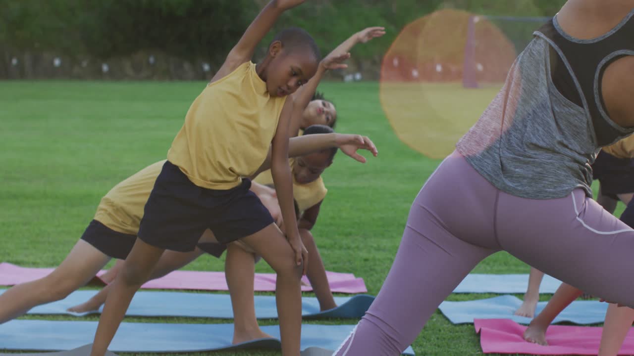 maestra de raza mixta que muestra a un grupo diverso de escolares ejercicios de estiramiento de yoga al aire libre