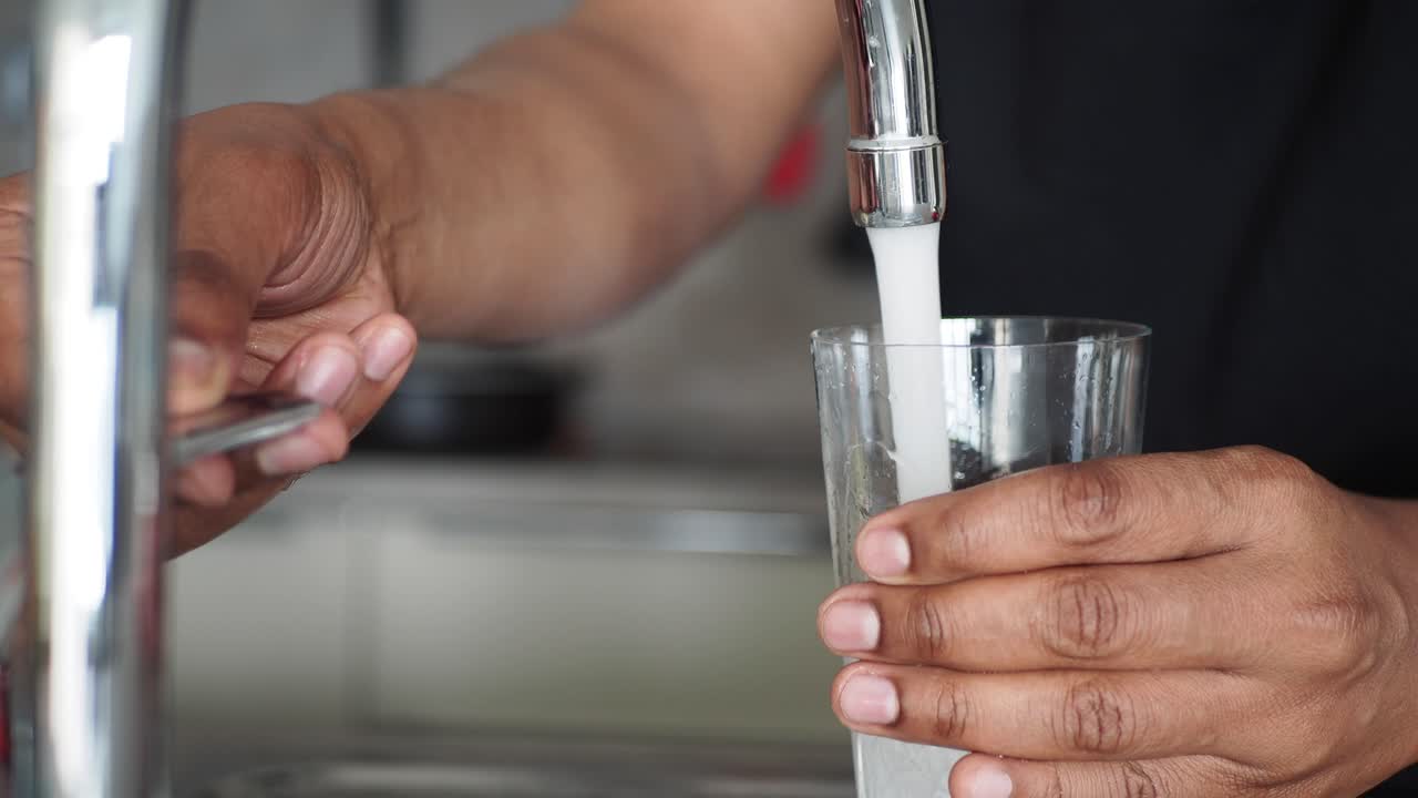 persona llenando un vaso con agua de un grifo de la cocina