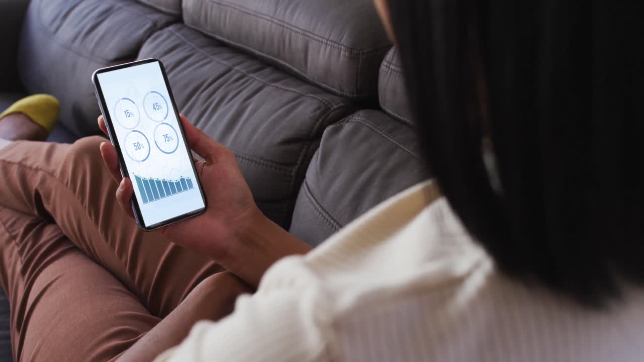 스크린에 통계를 가진 스마트 폰을 사용하여 소파에 앉아있는 혼합 인종 여성