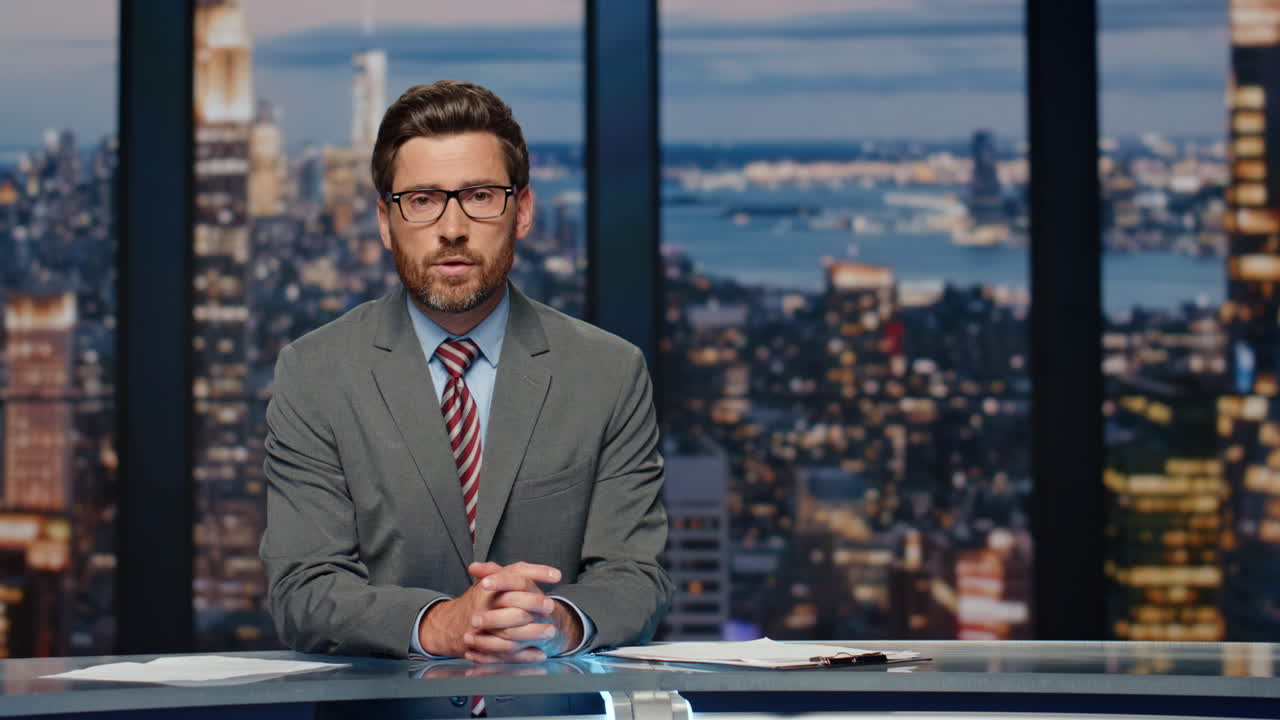 Nyhetsanker snakker om siste nytt sittende på scenen i et TV-studio. Mannen snakker.