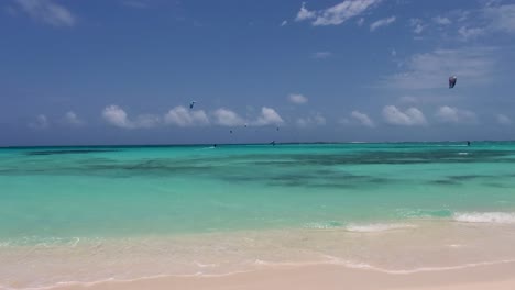 POV-watching-people-kitesurf-on-turquoise-caribbean-sea,-beautiful-shore-beach-scene
