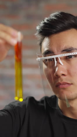asian medical student guy with mask looks at test tube with red and yellow separated liquids working in scientific chemical laboratory closeup