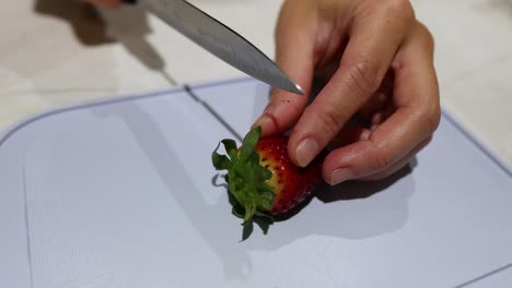 hands cutting a strawberry on a cutting board