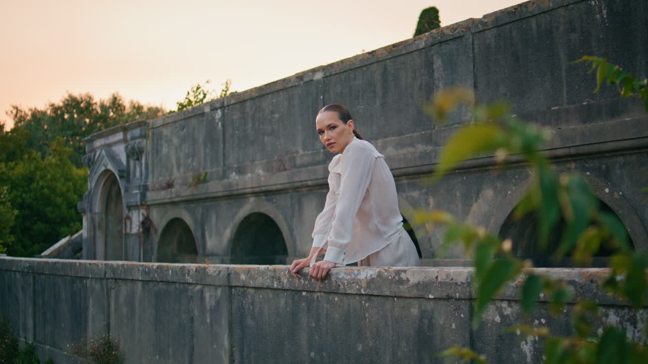 성의 발코니에서 포즈를 취하는 소녀 평온한 여름 저녁. 돌의 레일링에 기대어있는 여성