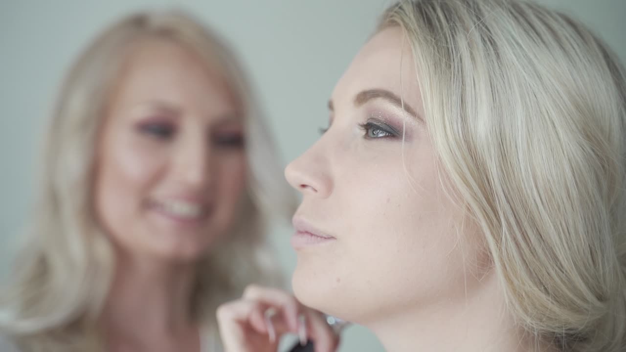 Make up artist at work apply powder to blond womens face both laughing and smiling - close medium shot