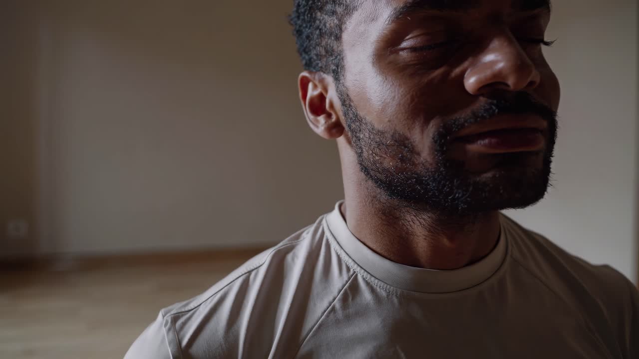 Young black man sitting in lotus position, practicing meditation with eyes closed, embodying serenity and inner peace within bright, minimalist room interior