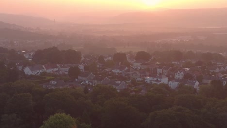 drone shot travelling left to right over houses mixed with trees with sun flare on horizon. aerial view of densely populated estates and streets at dawn