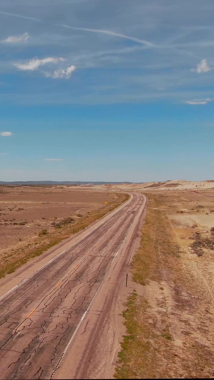 Uma longa rodovia se estende pela paisagem árida de Wyoming, emoldurada por céus azuis claros. Adequado para documentários de redes sociais ou vídeos verticais de viagens de carro.