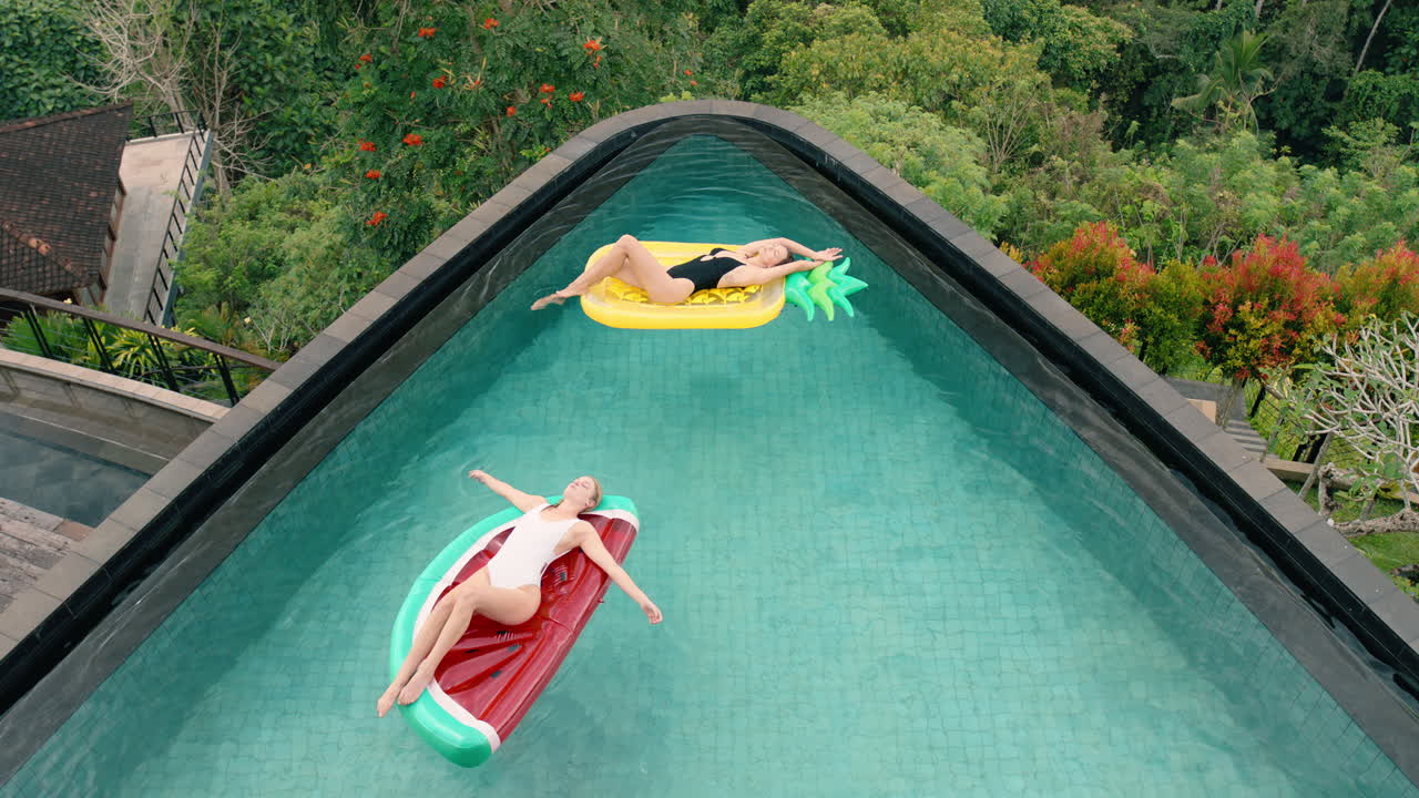 two women floating in swimming pool lying on inflatables best friends having fun summer day on vacation at tropical hotel resort wearing bikinis top view