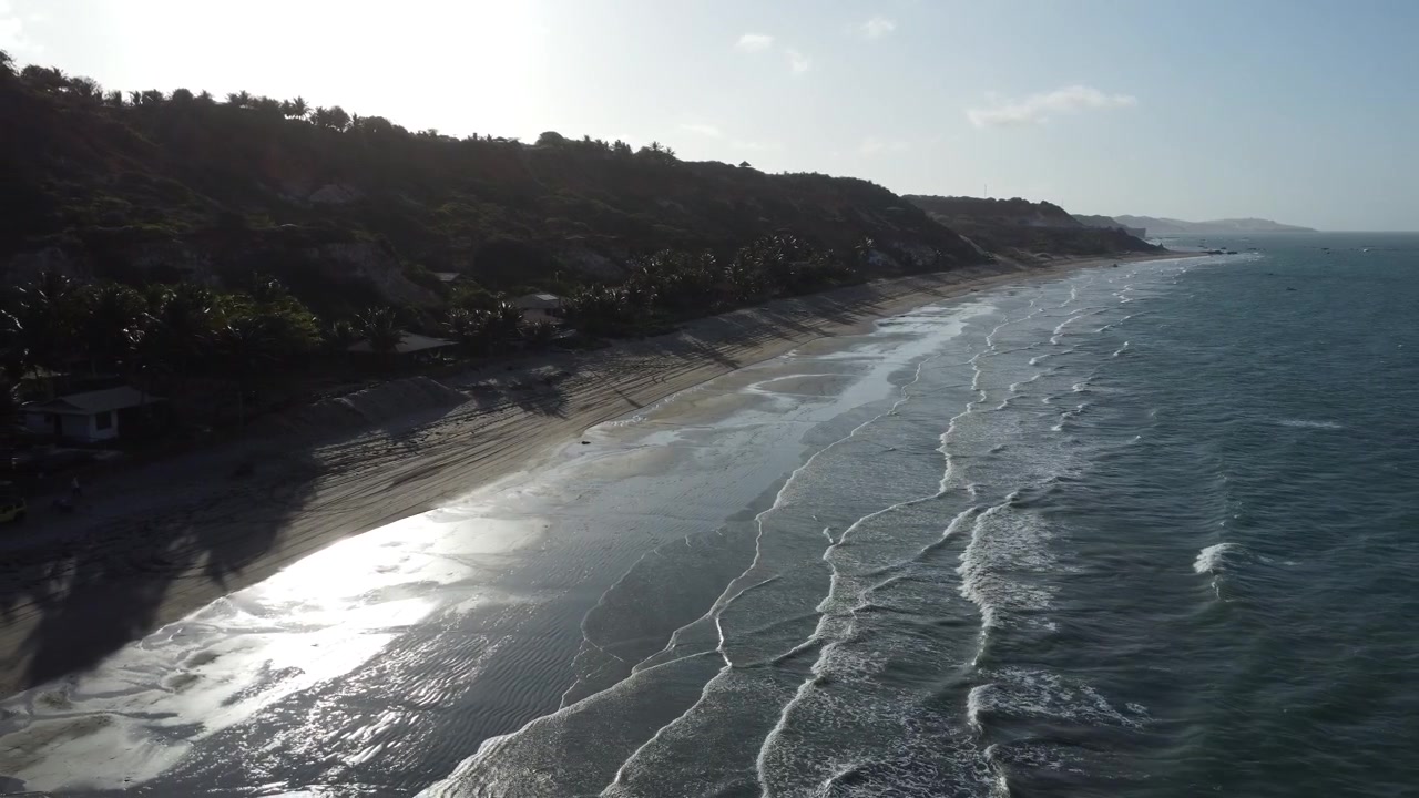 Drone che indietreggia sulla spiaggia all'alba, luce soffusa, onde calme che ondeggiano al vento