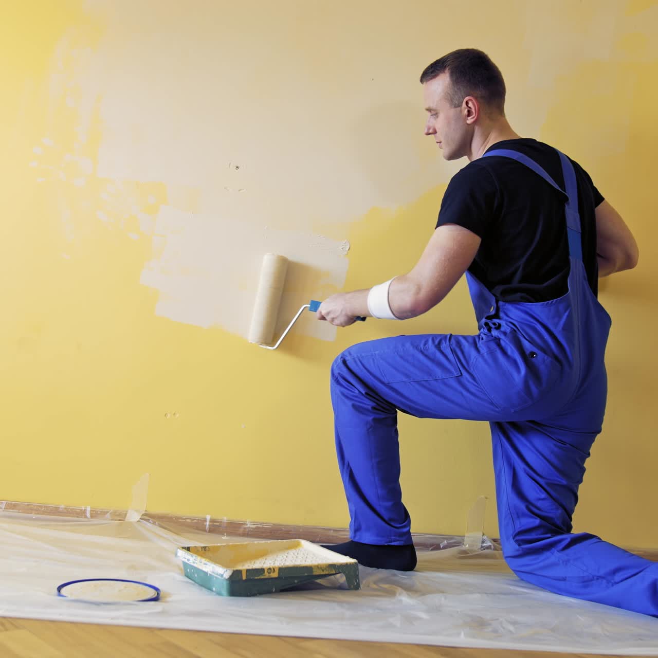 Young man painting wall with roller brush while renovating his apartment. Repair, building and home concept