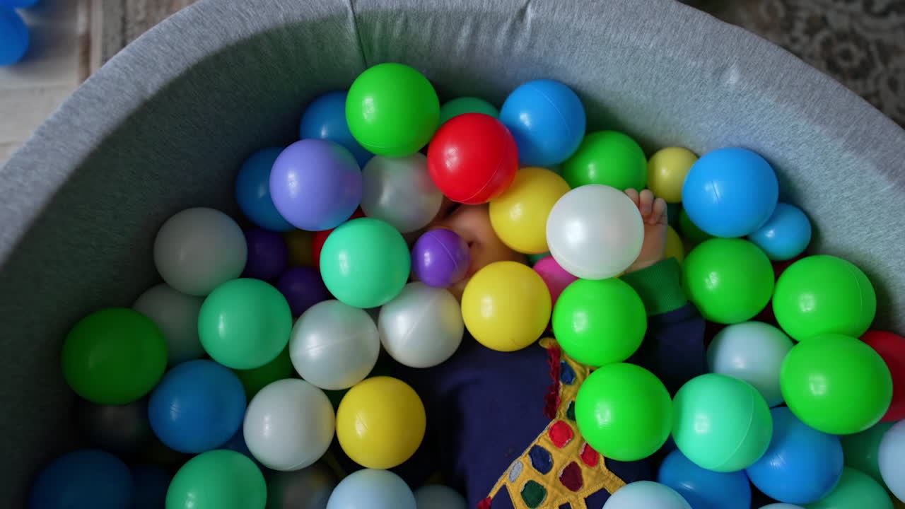 Unrecognized little boy lies half-covered with balls in the dry pool. Energetic kid moves actively in the basin. Top view.