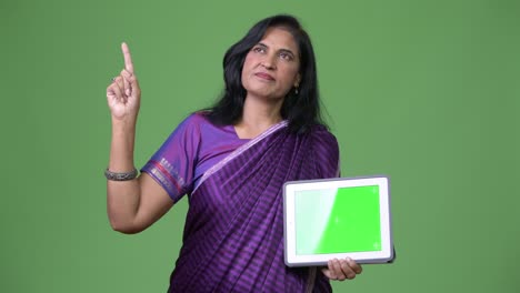 mature beautiful indian woman thinking while showing digital tablet and pointing finger up