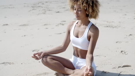 woman meditating on beach in lotus position