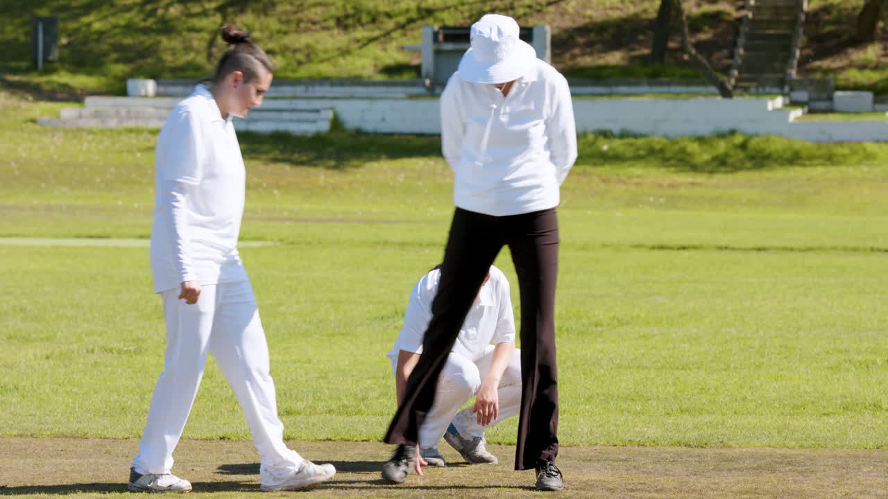 Playing cricket, female players and umpire inspecting pitch on sunny day