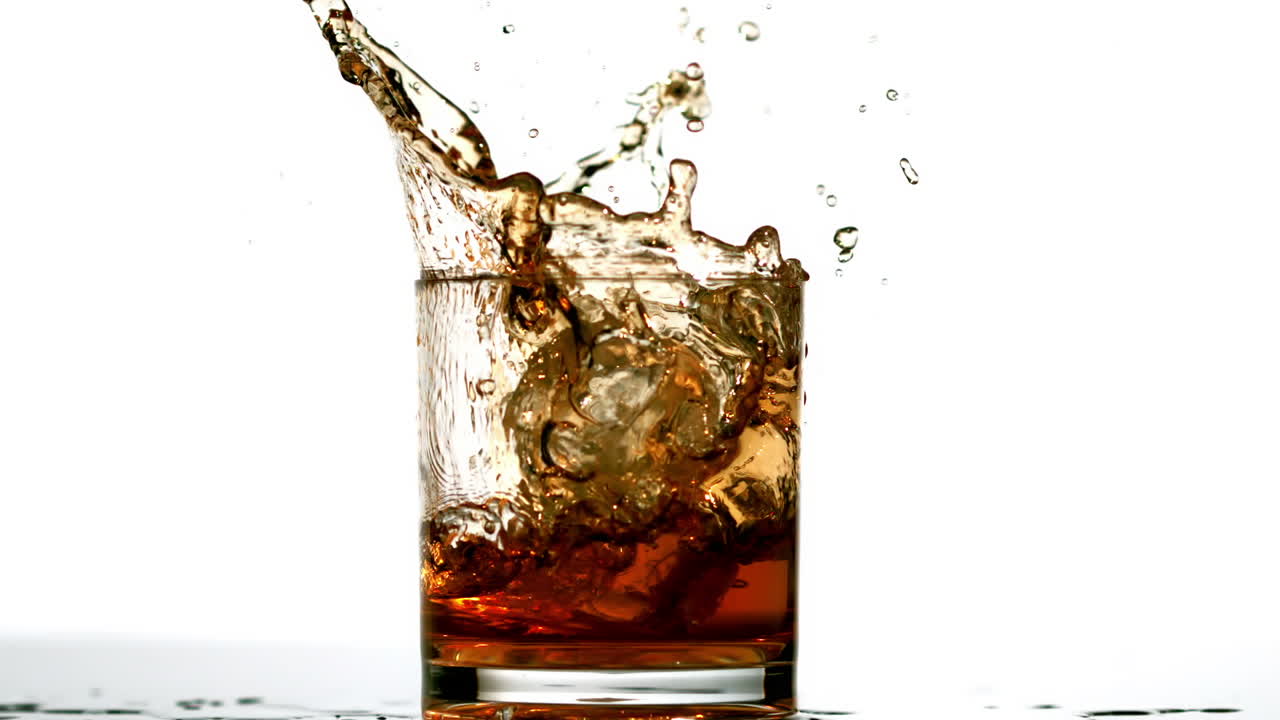 Cubetto di ghiaccio che cade in un tumbler da whisky su sfondo bianco