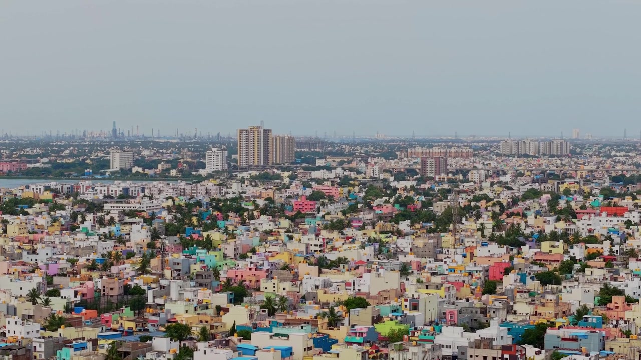 Vista aerea con drone di edifici residenziali colorati che coprono una densa area urbana, con grattacieli e uno skyline cittadino distante visibile attraverso Chennai, Tamil Nadu, India.