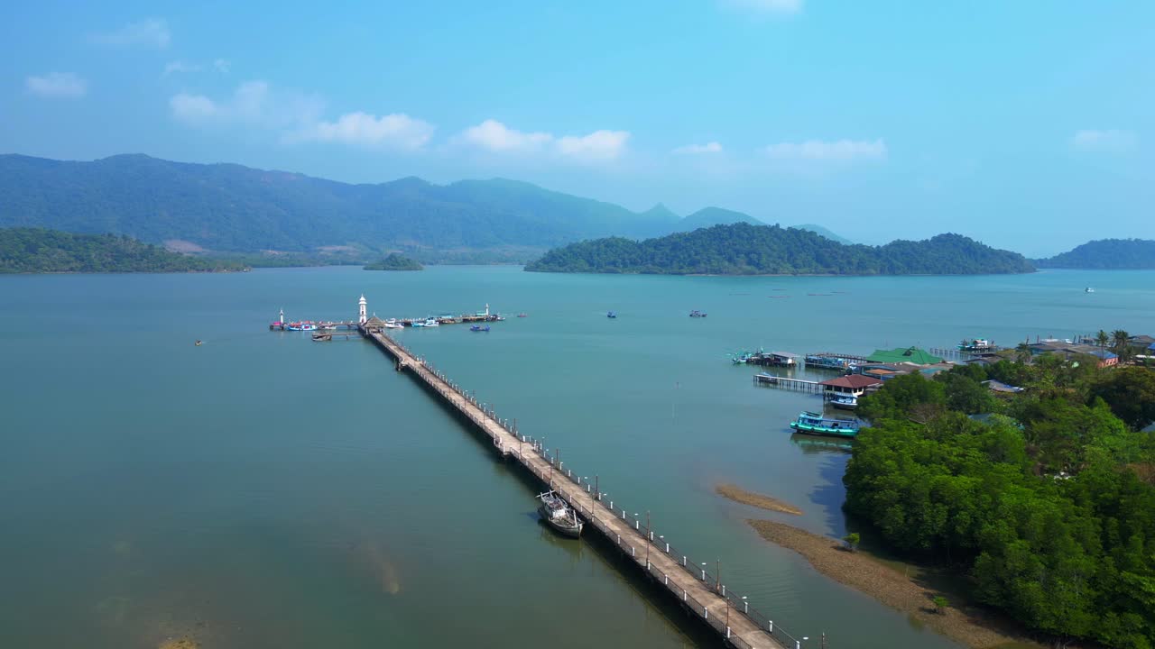 Coastal village with houses on stilts, boats and a long pier in a tropical bay. Unique aerial view descending drone