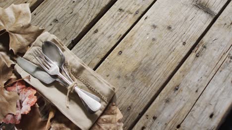 close up view of cutlery set over a napkin and autumn leaves with copy space on wooden surface