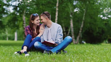 Junger-Mann-Und-Eine-Frau,-Die-Ein-Buch-Im-Park-Lesen,-Sitzen-Auf-Einem-Grünen-Rasen-HD-Video
