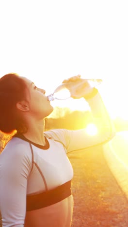 athletic woman drinking water during sunset while exercising outdoors in a vibrant environment