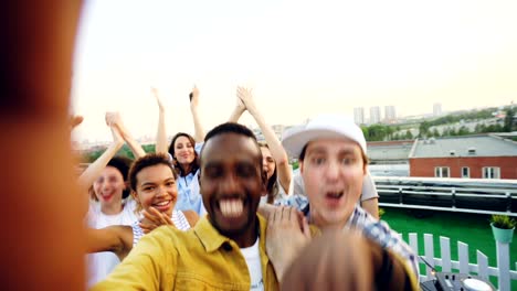 point of view shot of handsome african american man partying with friends on rooftop, dancing and having fun with drinks. sky and beautiful city is visible.