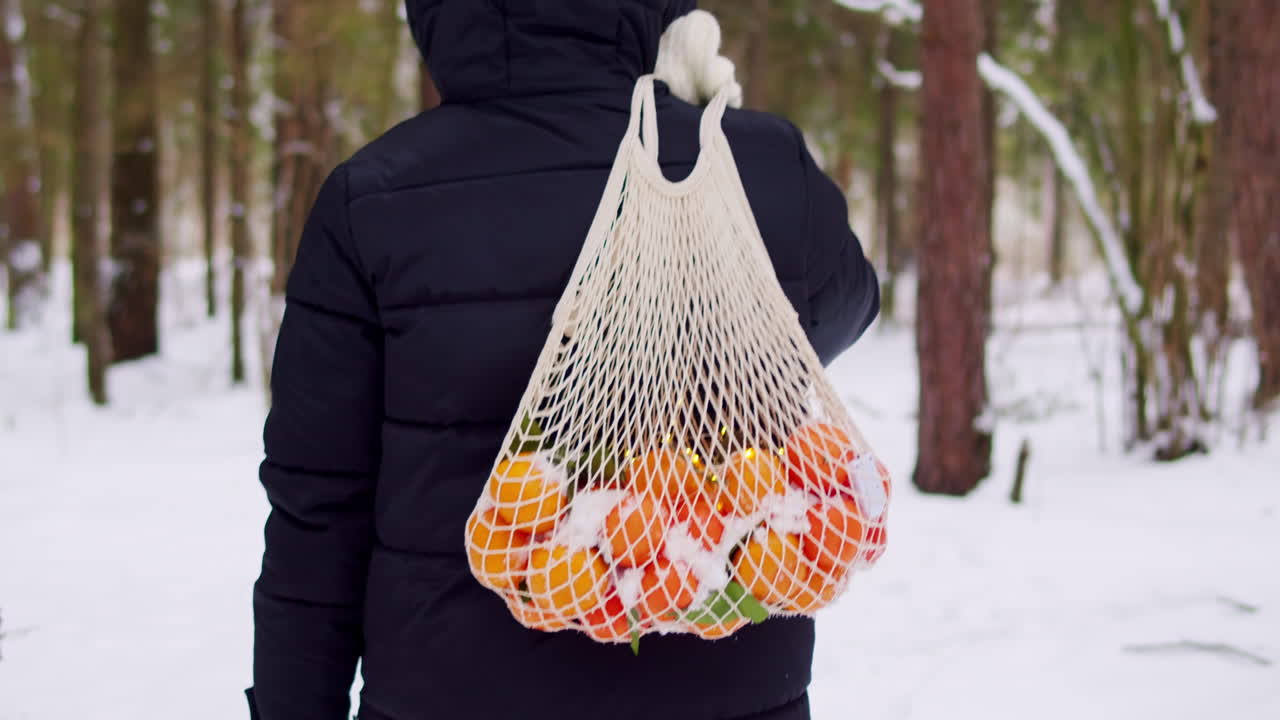 눈 인 숲 에서 망 가방 에 오렌지 를 들고 있는 사람