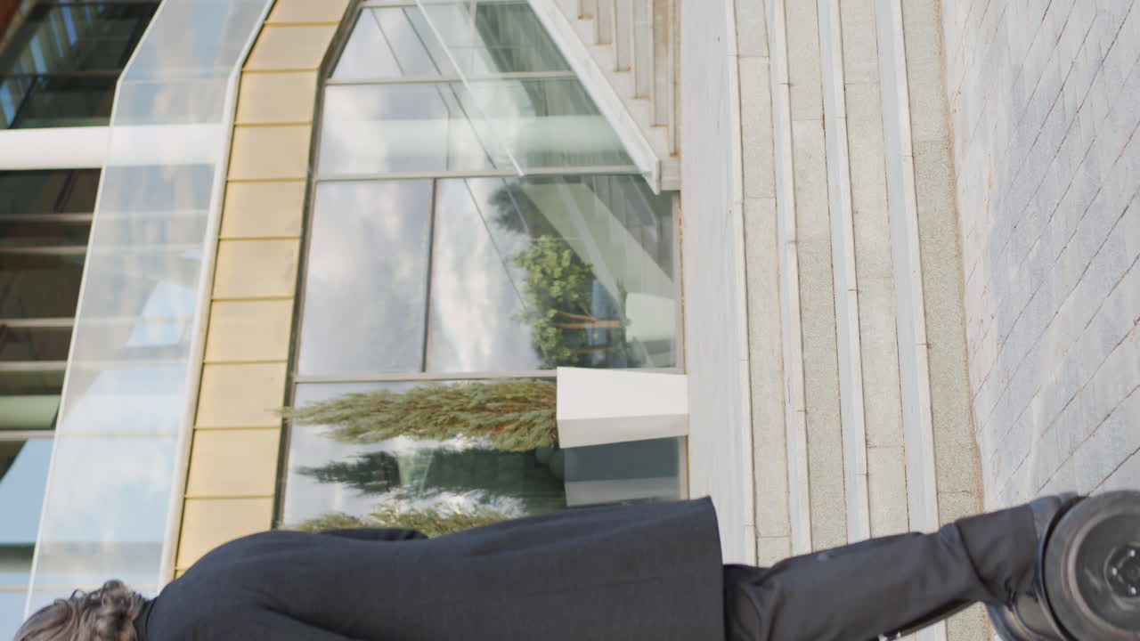 A stylish man with a beard uses a tablet while riding a self-balancing scooter in an urban setting