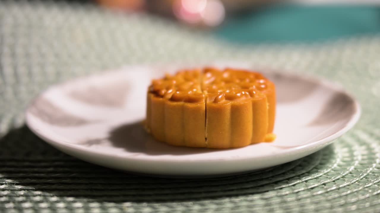 A traditional Chinese mooncake, a delicacy for the Mid-Autumn Festival, rests on a plate. It is scored down the middle, ready to be cut and shared as part of the celebration