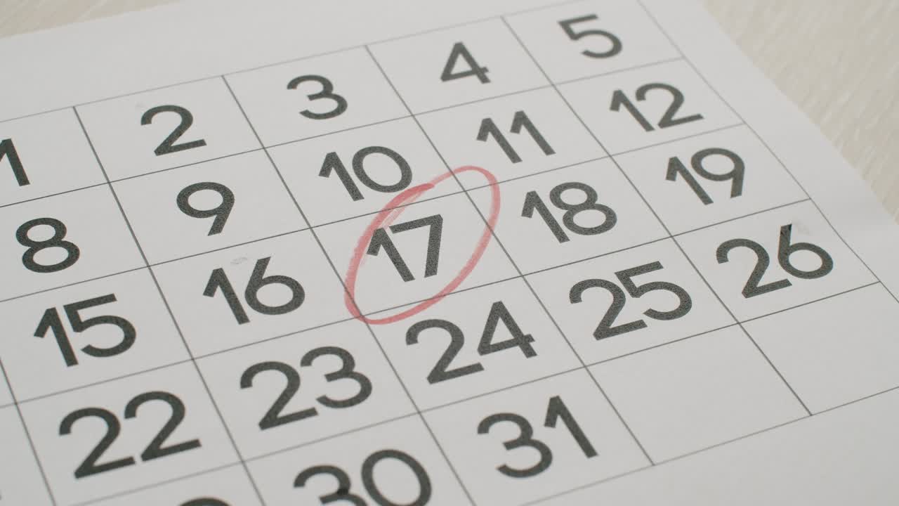 la mano del hombre escriba el día 17 en el calendario de papel usando un bolígrafo rojo.