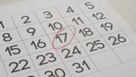 la mano del hombre escriba el día 17 en el calendario de papel usando un bolígrafo rojo.